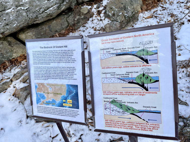 An outcrop of metamorphic rock with informational signs explaining the geologic history of the bedrock that forms Distant Hill.
