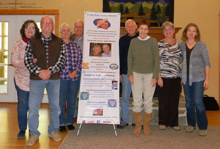 From Left: Jan and Jack Bazner, Judy and Dewey Gidcumb, Gerry and Cheryl Cline, Laura Bell and Holy Turner. They are standing around a poster for Living with Victory, a radio ministry that Mountain Top Experience supports.