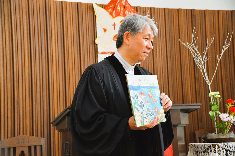 2026年6月14日 創世記1章「せかいのはじまり」の紙芝居を手にメッセージする森牧師