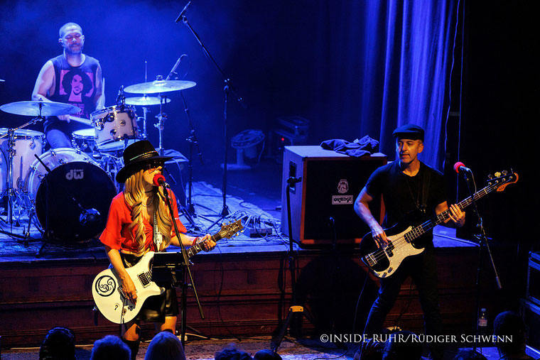 <img src="beispielbild.jpg" alt="Orianthi on stage at Musiktheater Piano, wearing a red lace top, knee-high boots, a hat and sunglasses, playing an electric guitar">