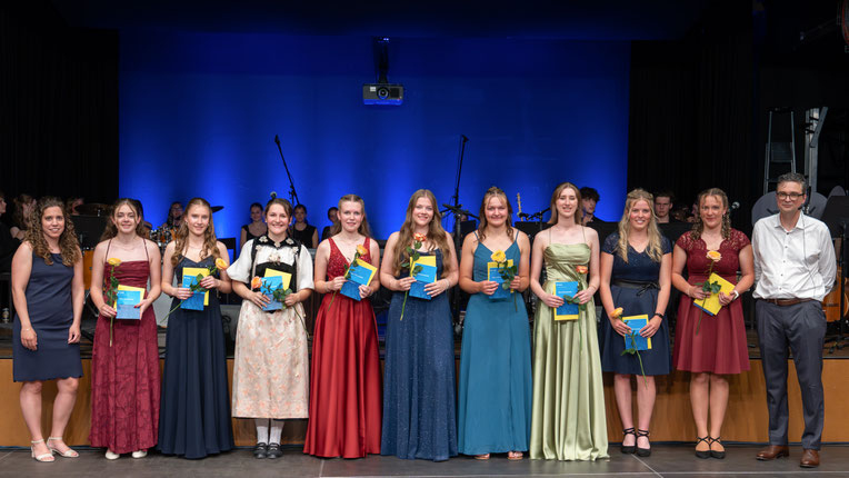 Gruppenfoto der Maturitätsklasse K22 der Kantonsschule Schüpfheim mit Maturazeugnissen und Rosen auf der Bühne bei der Maturafeier 2026.