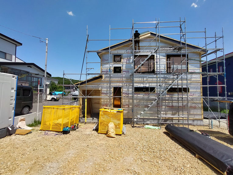 建築中の住宅正面に足場が組まれ、作業員が上部で外壁作業の準備をしている様子。
