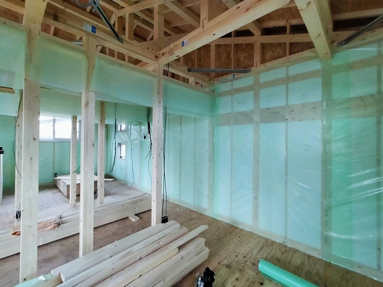 木造住宅の2階 構造材と外壁内側に、緑色の気密シートが隙間なく施工されている室内の写真