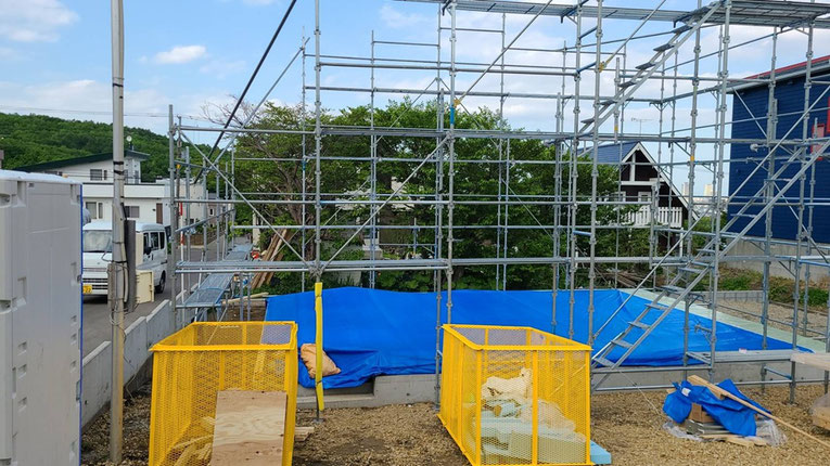 足場が組まれた敷地内に、ブルーシートで覆われた基礎部分