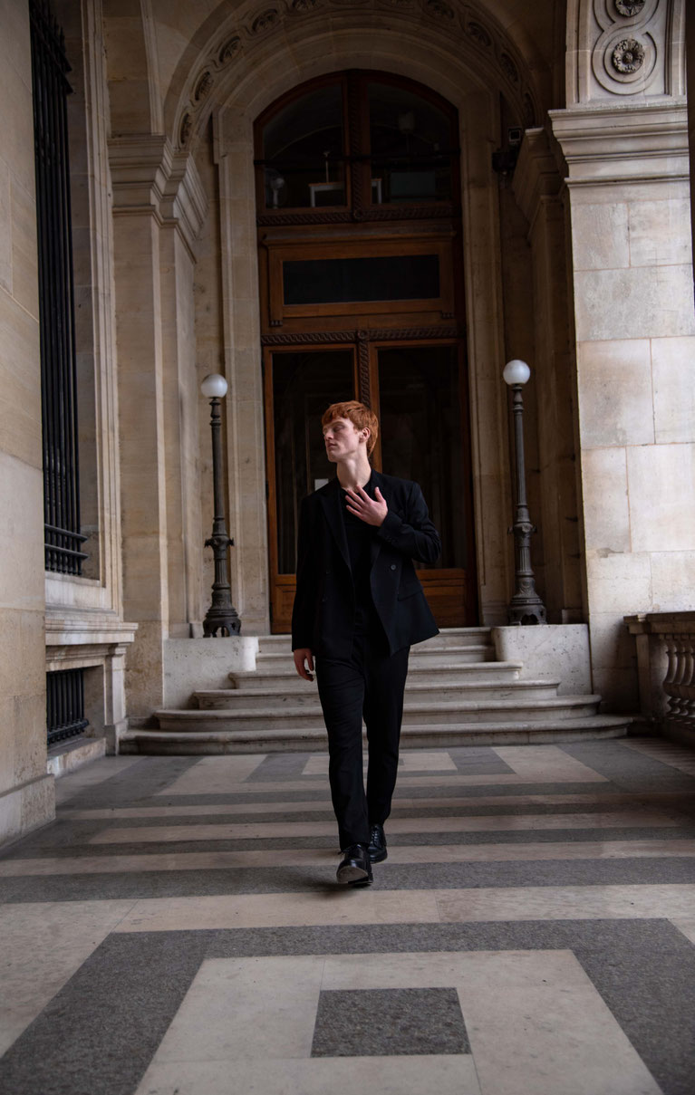 Color fashion portrait of a professional male model with red hair in motion blur, wearing a blazer realized next to the louvre