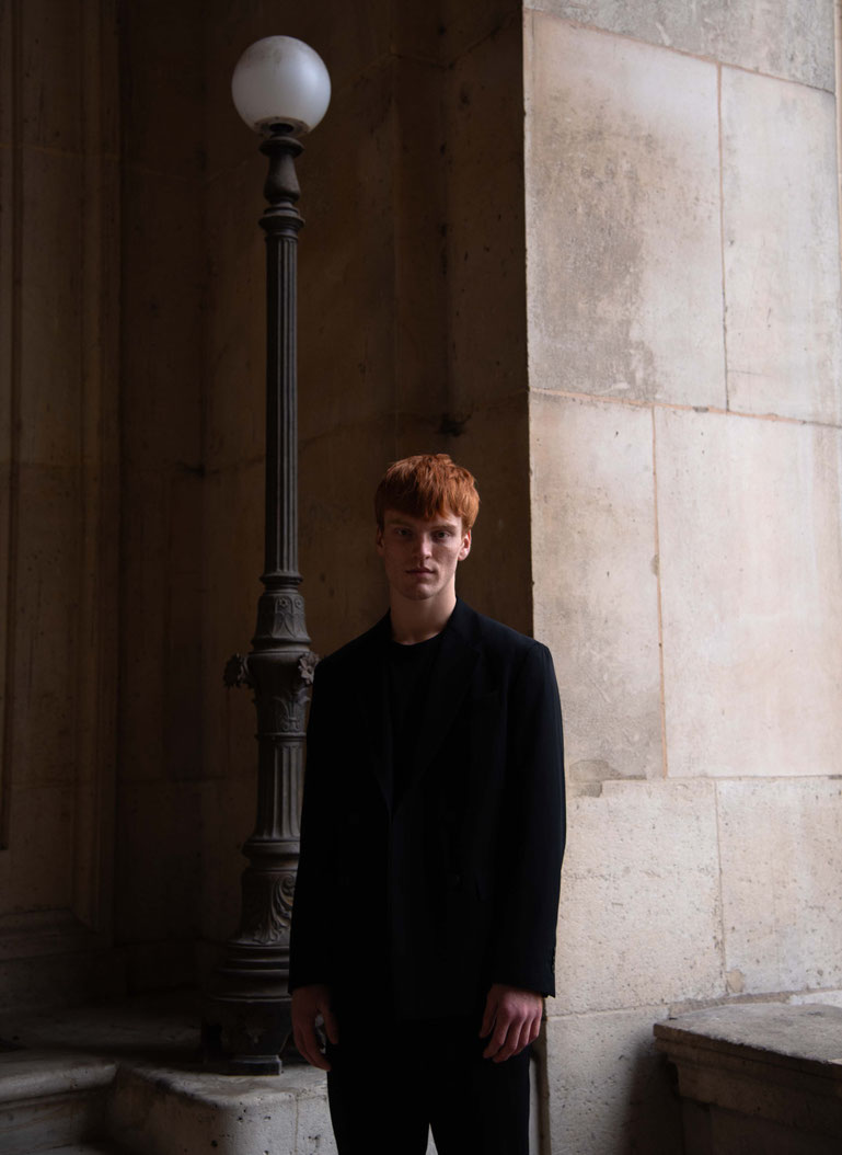 Color fashion portrait of a professional male model with red hair in motion blur, wearing a blazer realized next to the louvre
