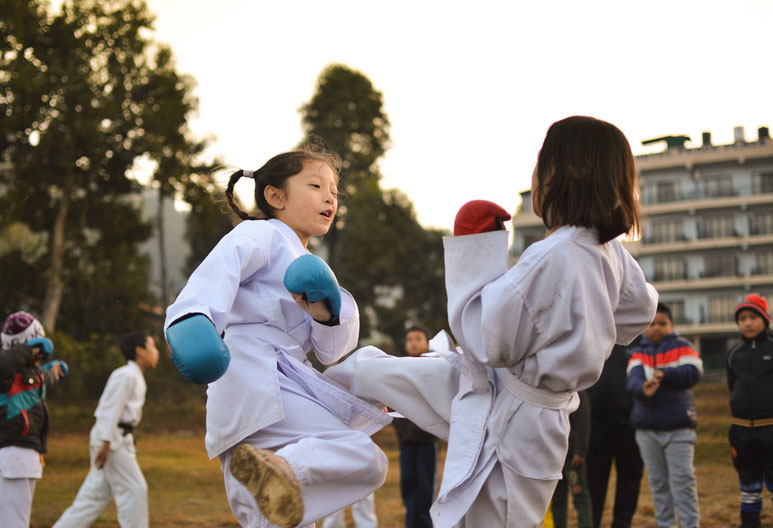 Zwei Kinder trainieren Karate. Das Mädchen mit den roten Boxhandschuhen tritt das Mädchen mit den blauen Boxhandschuhen.