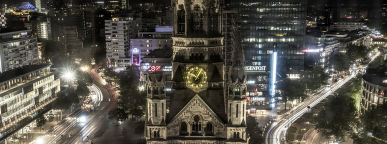 Nachtaufnahme mit Spiegelungen Kaiser-Wilhelm-Gedächtnis Kirche  in Berlin als Farbfotografie im Panorama-Format