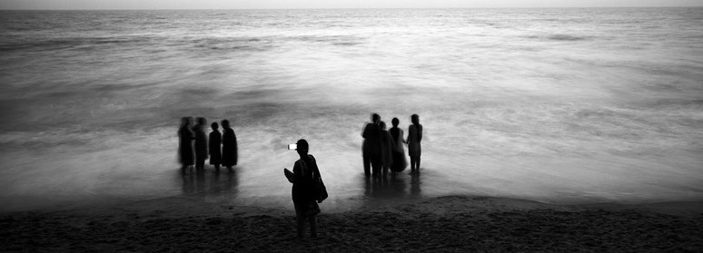 Lehrer fotografiert mit Mobiltelefon in der Dämmerung Schülerinnen am Strand in schwarz-weiß als Panorama-Photographie