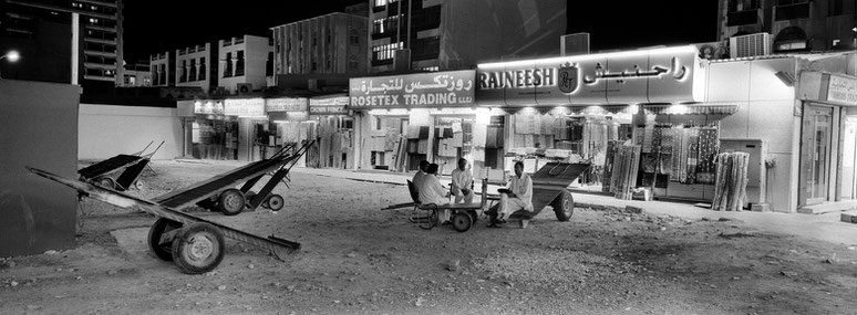 Vier Männer sitzen auf Sackkarren im Souk in Dubai als Panorama-Photographie