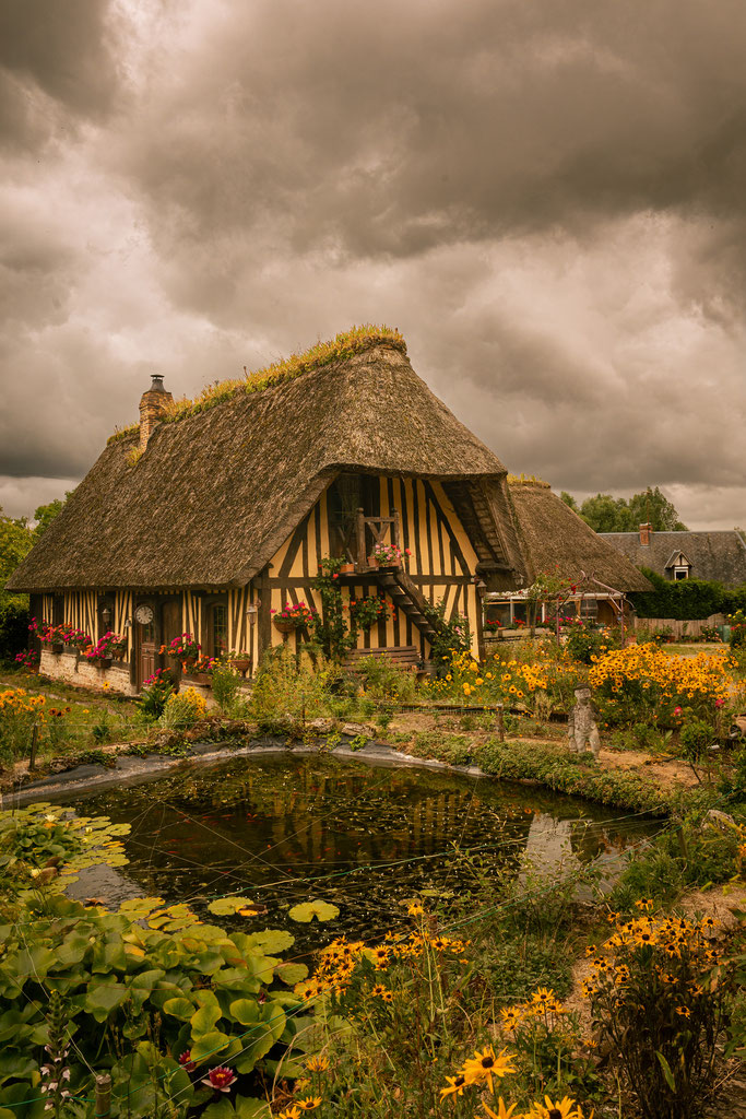 Ein Fachwerkhaus spiegelt sich im Gartenteich auf der Route des Chaumières in der Normandie. 