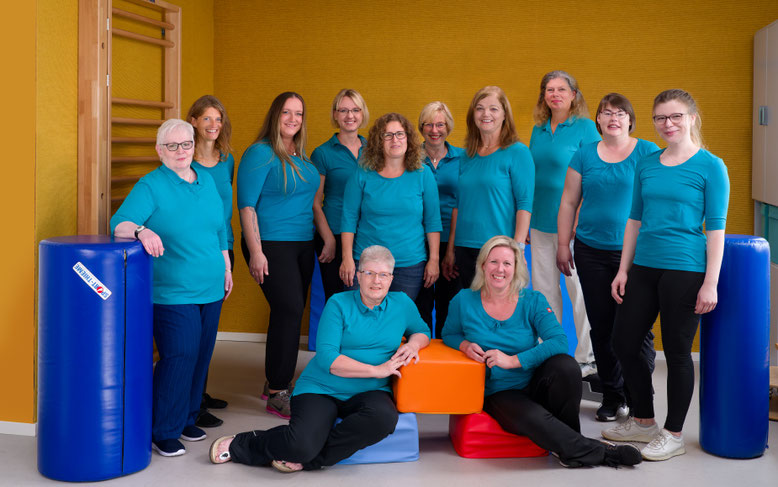 Foto vom gesamten Team der Physio-Praxis Baden mit blauen Oberteilen in einem Trainingsraum der Praxis.