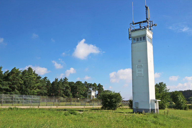 DDR-Grenzturm mit dem Eingang rechts in Richtung Thüringen orientiert. Im Bildhintergrund der ehemalige US-Kontrollturm.