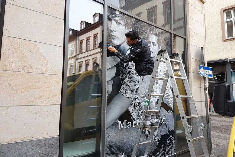 Anbringung einer Schaufensterbeklebung mit Modekampagne in Heidelberg Innenstadt