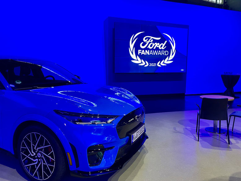 Ein blauer Ford Mustang Mach-E GT vor dem Logo vom Ford Fan Award