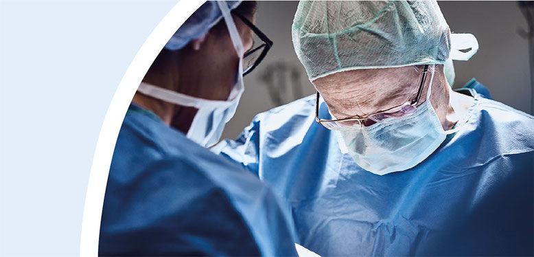 Chirurgisches Team, das in OP-Kleidung bei einer Operation konzentriert arbeitet, mit Fokus auf eine Person, die sich über den Patienten beugt.