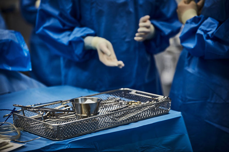 Vorbereitung für eine Operation: Medizinisches Personal in blauen OP-Kitteln steht um einen Tisch mit steril abgelegten chirurgischen Instrumenten.
