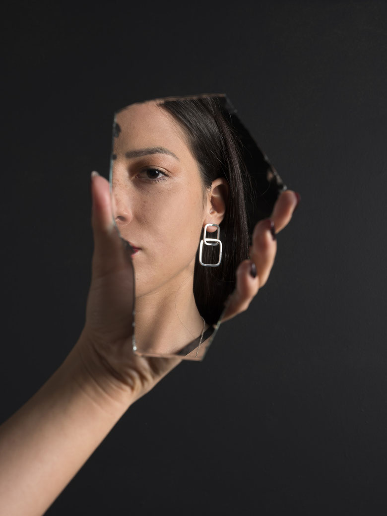 visage de femme se regardant dans un miroir portant une boucle d'oreilles Q10 en argent recyclé