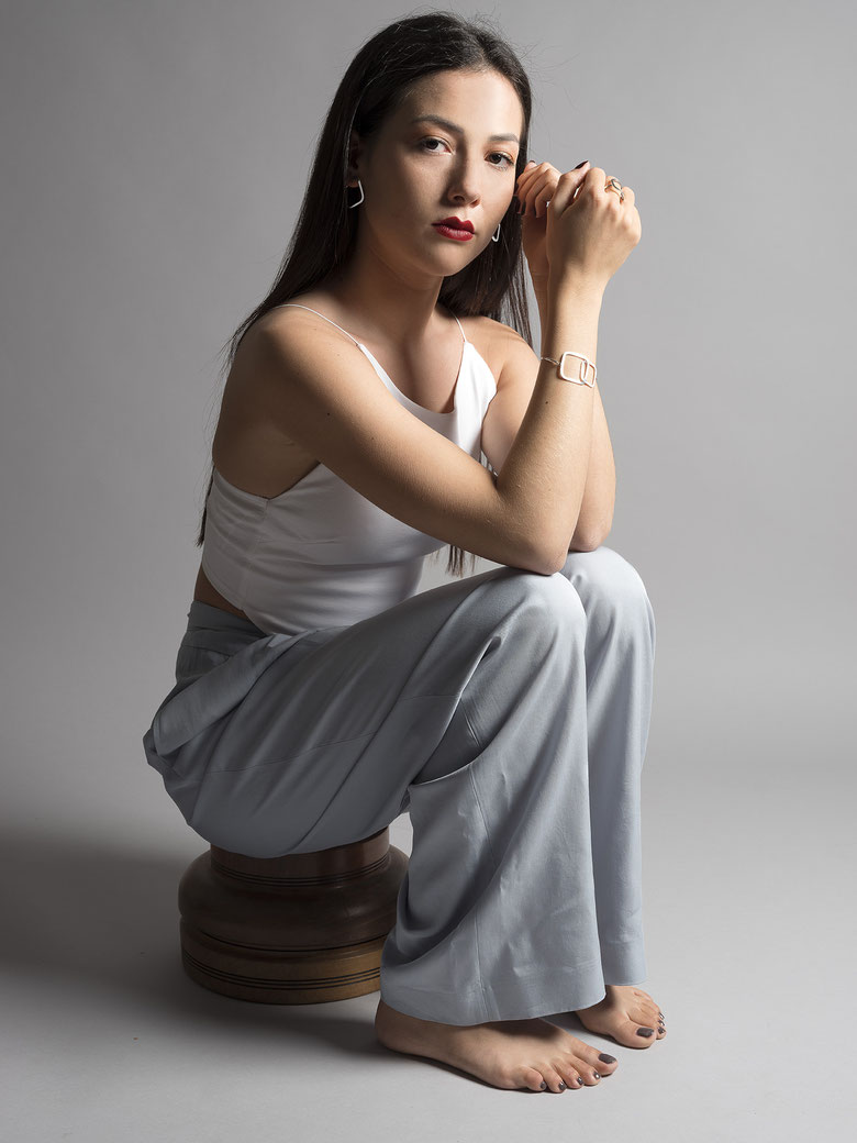 jeune femme assise sur tabouret en bois habillée d'un top blanc et pantalon large bleu portant un bracelet Q06 et des boucles d'oreilles Q09 en argent recyclé de la collection Quadra