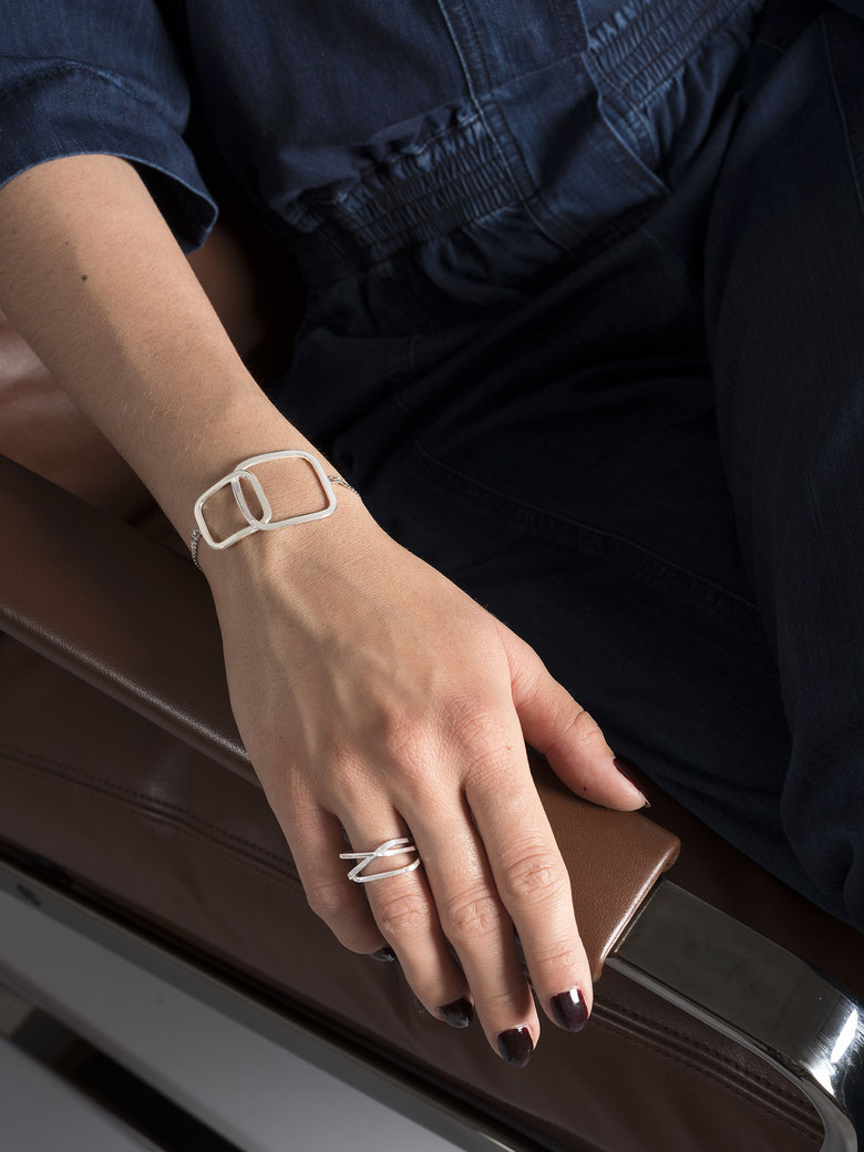 main de femme accoudée à un siège en cuir brun portant un bracelet Q06 et une bague Q02 en argent recyclé de la collection Quadra