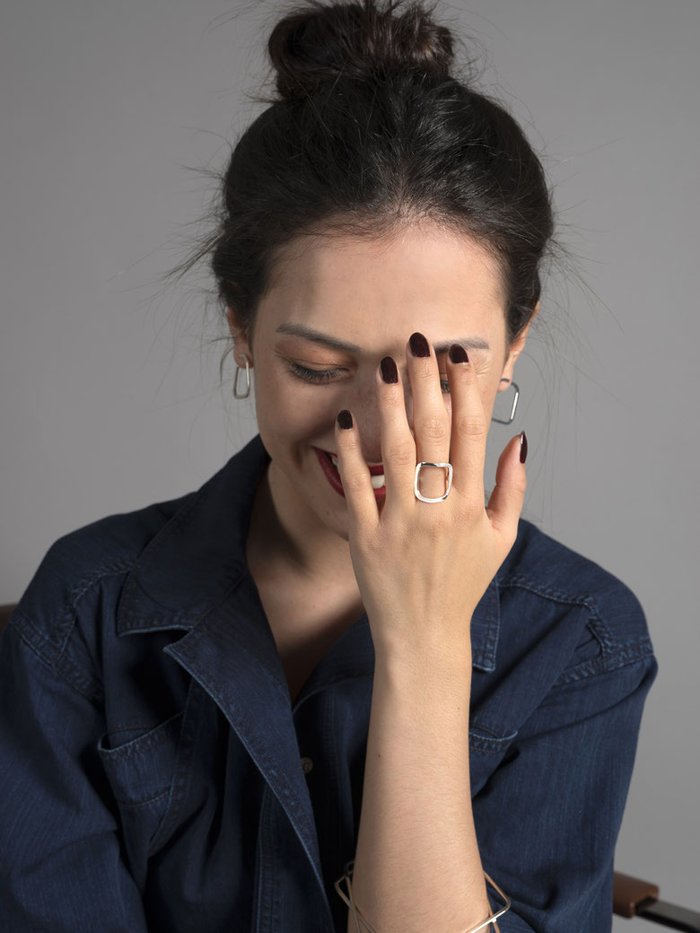 jeune femme souriante avec sa main devant son visage qui porte une bague Q01 et des boucles d'oreilles Q09 de la collection Quadra