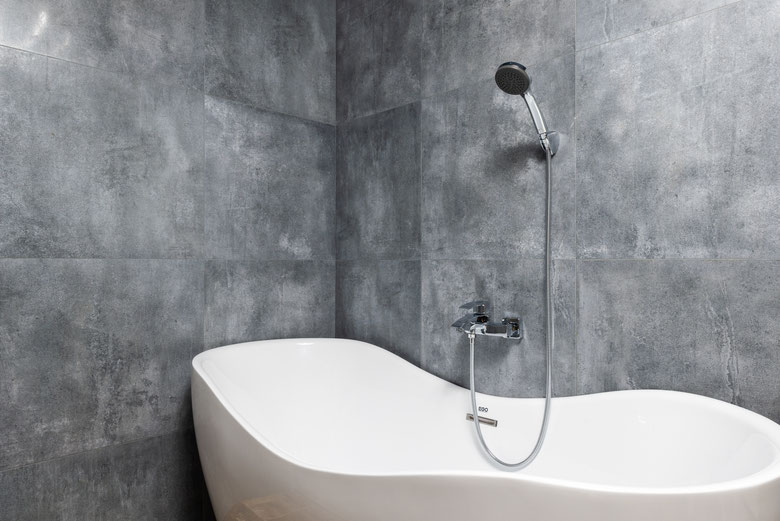 Bathroom interior with bathtub under shower on marble like tile wall