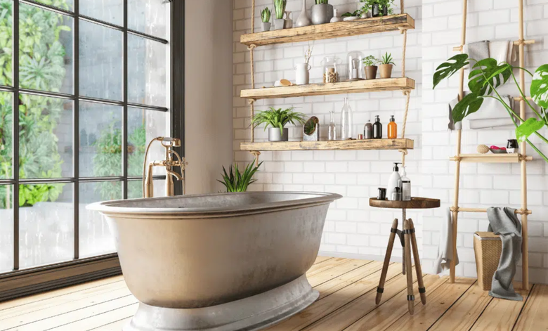 This image showcases a stylish and tranquil bathroom with a vintage freestanding tub, large windows offering natural light, wooden shelves adorned with plants and decor, and a minimalist wooden stool holding bath essentials.