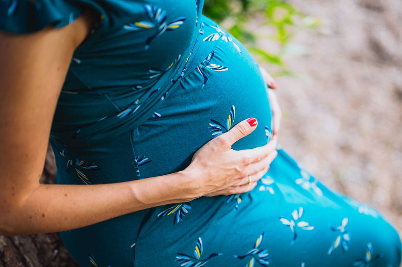 Werdende Mutter hält im Sitzen ihren Babybauch fest.