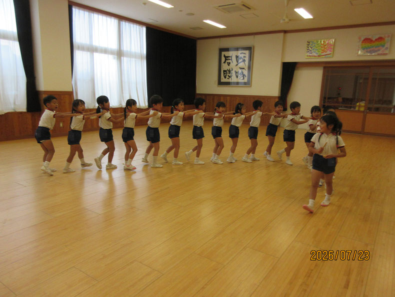 いつもは暗誦で遊んできましたが、今日は先頭と尻尾を決めて繋がり遊びをしました。生き生きとした 子ども達の表情が嬉しいです。先頭の子どもは拍子木でリズムをとっています