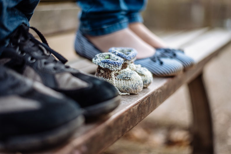 Zwischen den Schuhen der Eltern stehen die ersten Schuhe des Babys.