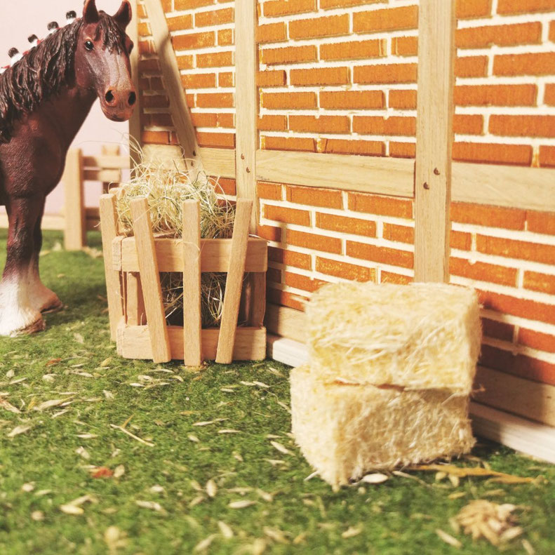 Spielszene eines Schleich® Pferdes vor Stall mit Heuraufe und Strohballen