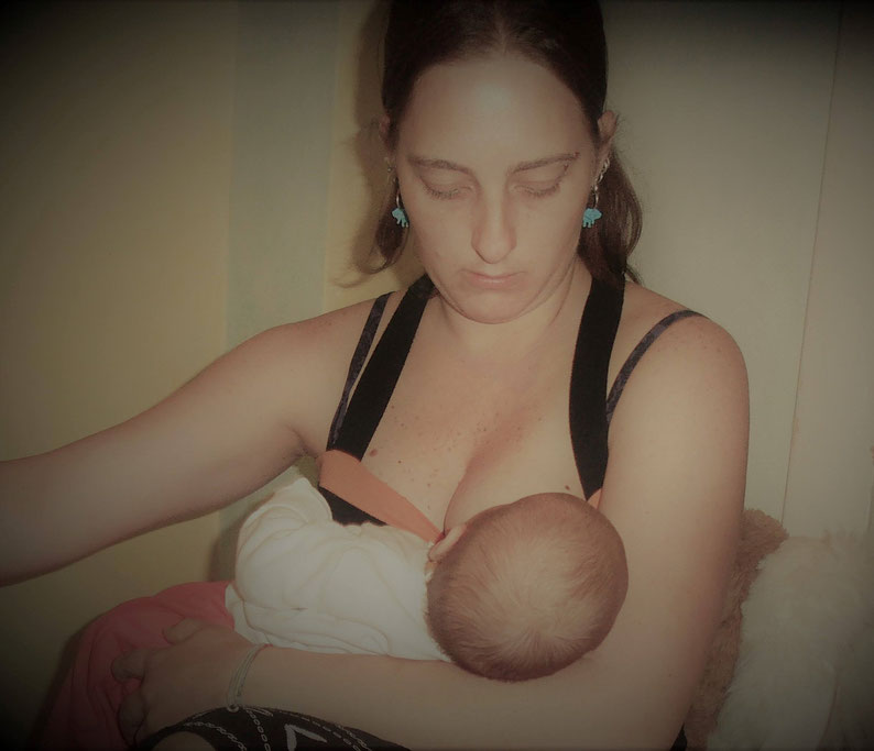 A breastfeeding woman and baby, mom looking at baby on her breast.