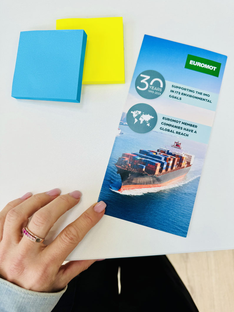 Hand hält ein EUROMOT-Flyer mit Containerschiff, daneben farbige Haftnotizen – visuelles Beispiel für Printdesign und Kommunikationsmaterial.