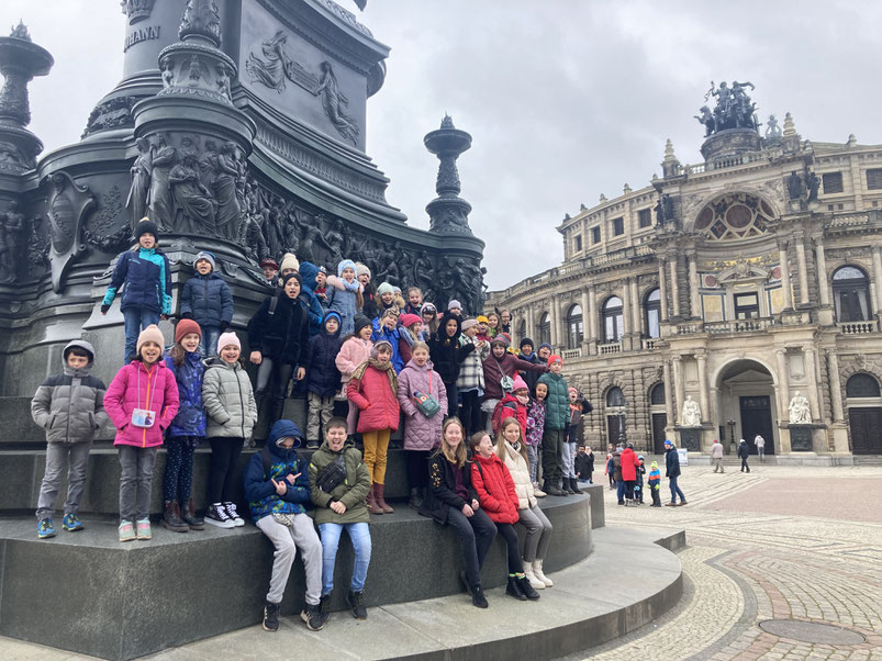 Auf dem Foto sieht man etwa 50 Kinder aus dem Musaik-Orchester auf dem Dresdner Theaterplatz mit der Semperoper im Hintergrund.