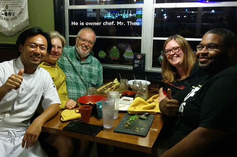 レストランのテーブルでシェフとお客さんたちが笑顔で記念撮影をしている様子。サンフォードの街には地元の名店が多く、観光客にも人気。オクトーバーフェストやドイツ料理店「ホラーバックス・ジャーマン・レストラン」などでにぎわうエリアで、温かい雰囲気と活気が魅力の街並み。