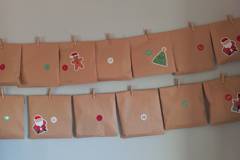 Ein selbst gebastelter Adventskalender aus braunen Papiertüten hängt in zwei Reihen an der Wand, es sind vereinzelt Aufkleber auf den Tütchen