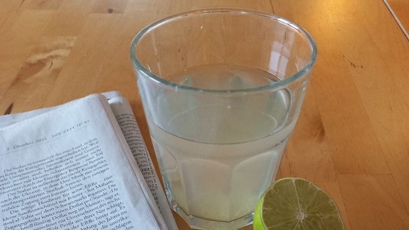 Glas mit Zitronentee steht auf dem Tisch, daneben eine halbe Zitrone und Zeitung