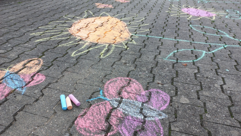 Mit Straßenmalkreide auf das Hofpflaster gemalte Schmetterlinge in lila und weiß, dahinter eine große gemalte Blume