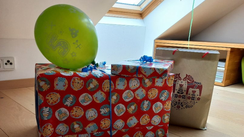 Geschenke stehen nebeneinander, auf einem liegt ein grüner Luftballon mit der Zahl fünf darauf