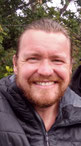 Das Bild Robert Mehl. Er ist Diplom-Psychologe und Kriminologe. Er hat einen Bart und trägt seine längeren Haare zusammengebunden. Auf dem Bild lacht er in die Kamera und trägt eine dunkle Daunenjacke.