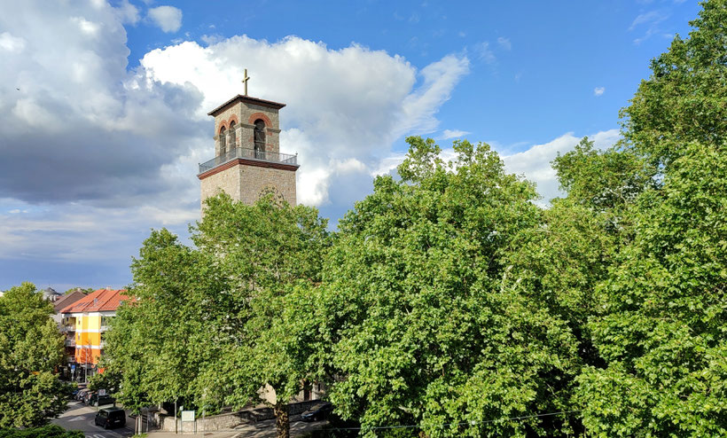 Turm der Lutherkirche Bruchsal mit den Bäumen des Luisenparks im Vordergrund.