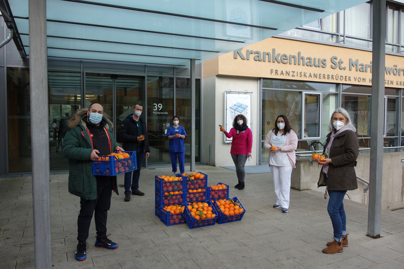 von links) Dem Orangenspender Moreno Pochiera dankend sehr herzlich die Stellvertretenden aus dem Pflegeteam Jan Meier, Johanna Weber, Anja Herbst-Kaluza und Gülnur Özkiran, daneben Unterstützerin der Aktion Ayse Jung Foto: Franziskanerbrüder vom Heiligen