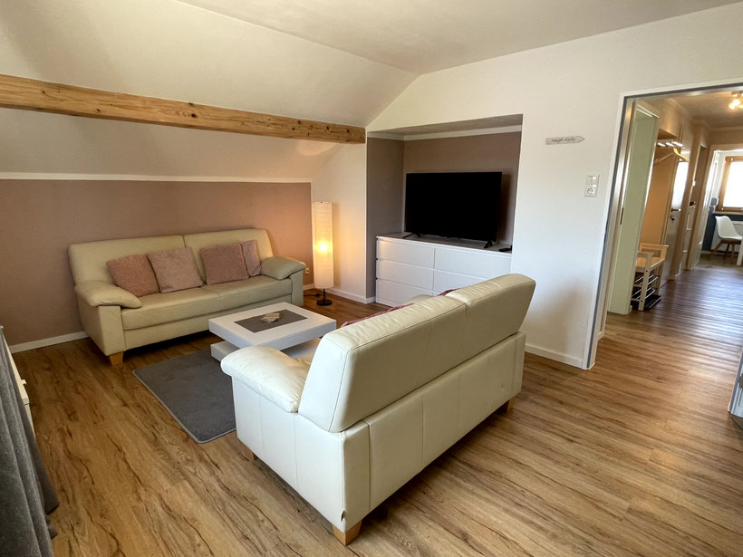 Wohnraum mit naturweißen Ledercouchen und weißem Couchtisch, Ambiente-Stehleuchte, in einer großen Nische Flatscreen 50 Zoll auf weißer Kommode, weiße und altrosafarbene Wände