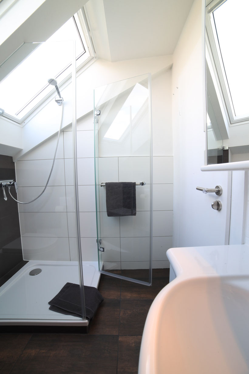Glasdusche mit niedrigem Einstieg unter Dachflächenfenster, Bodenfliesen in Mooreiche, Wandfliesen weiß, dunkelbraune Handtücher, Tür weiß lackiert