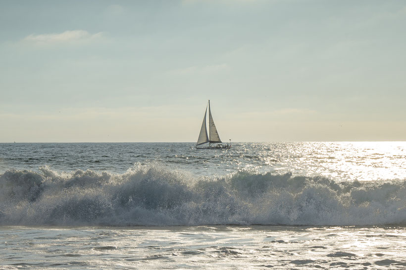 A sailing boat passing by along the shore of Manhattan Beach, California