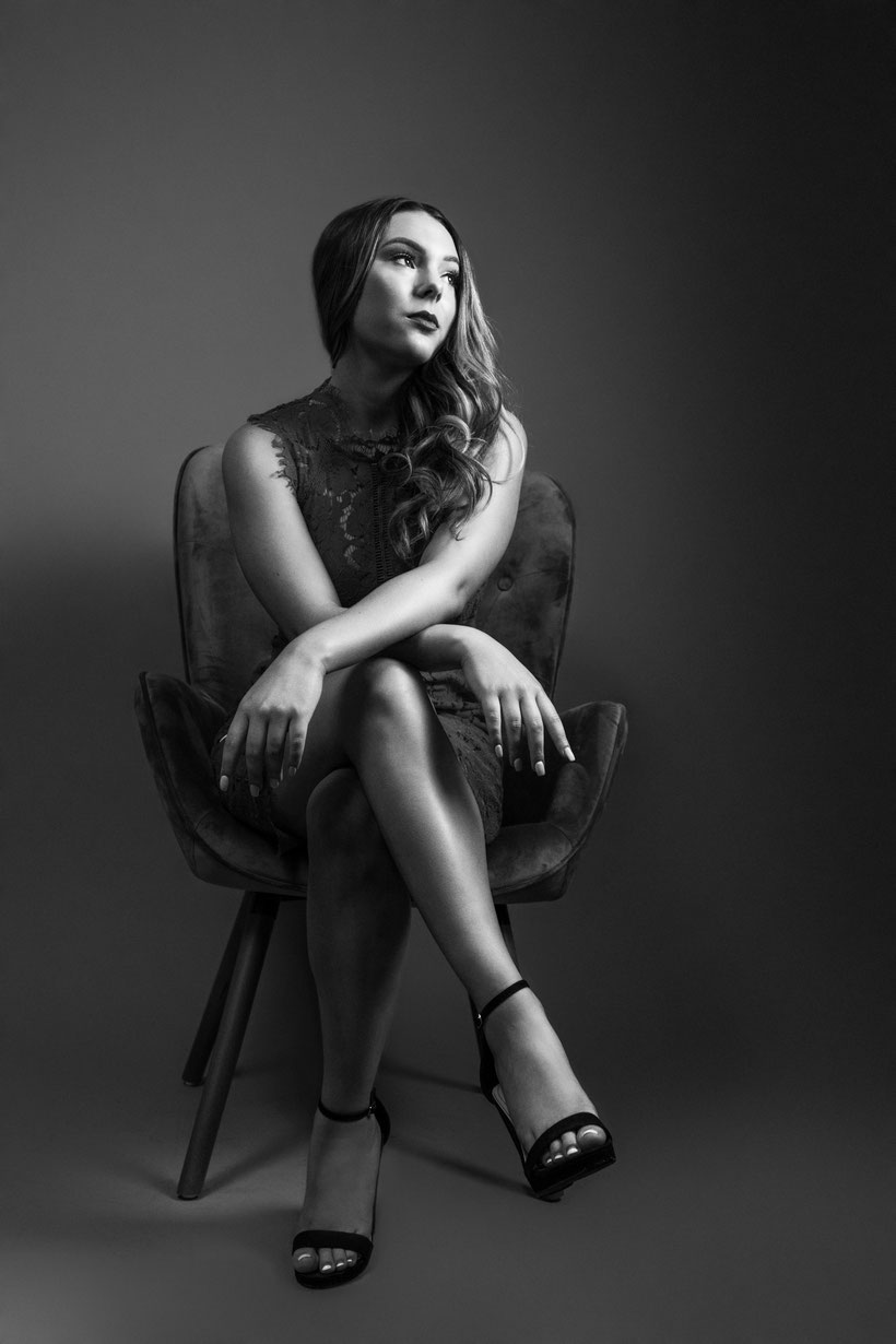 black and white image young teen girl sitting with legs crossed and arms crossed over knee looking up to the right at the light, deep in thought