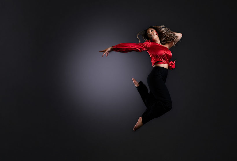 high school girl in black pants and red one sleeved silky top jumping mid air and pointing back behind her