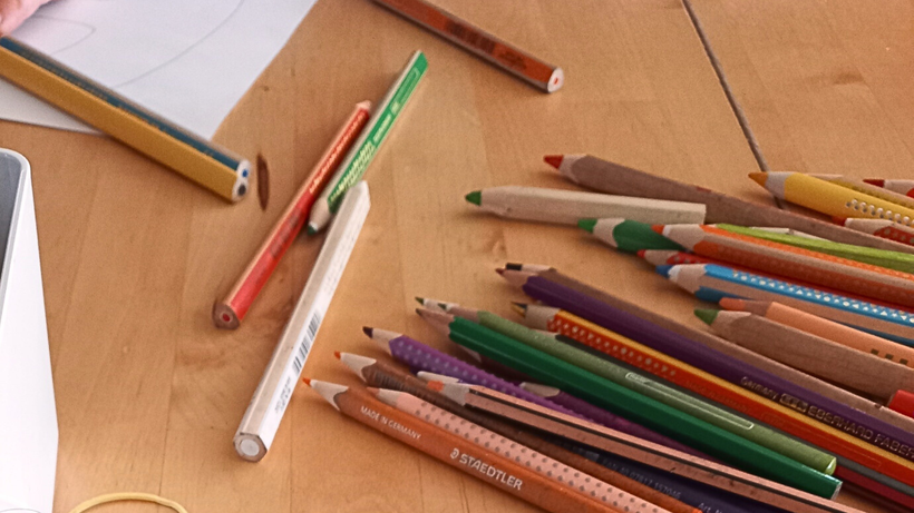 Bunte Stifte auf einem Tisch, daneben weißes Papier.