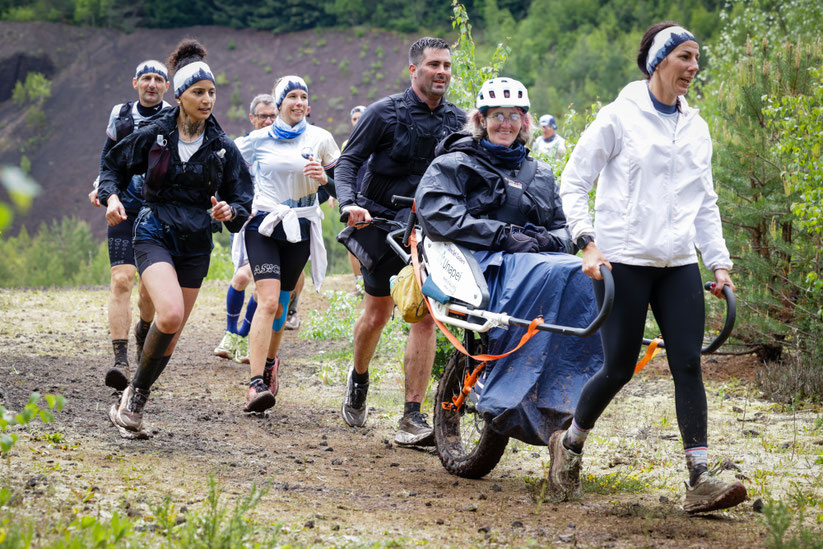 Équipe accompagnant une joëlette sur le parcours de la Volvic Volcanic Experience illustration des valeurs d'inclusion du trail