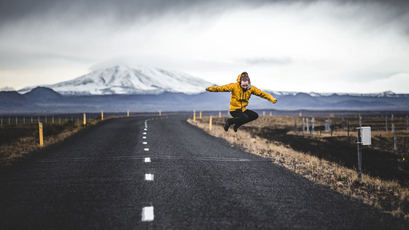 Junger Mann in gelber Trainingsjacke springt auf asphaltierter Straße in Island. Bild von Madara Parma auf Unsplash.